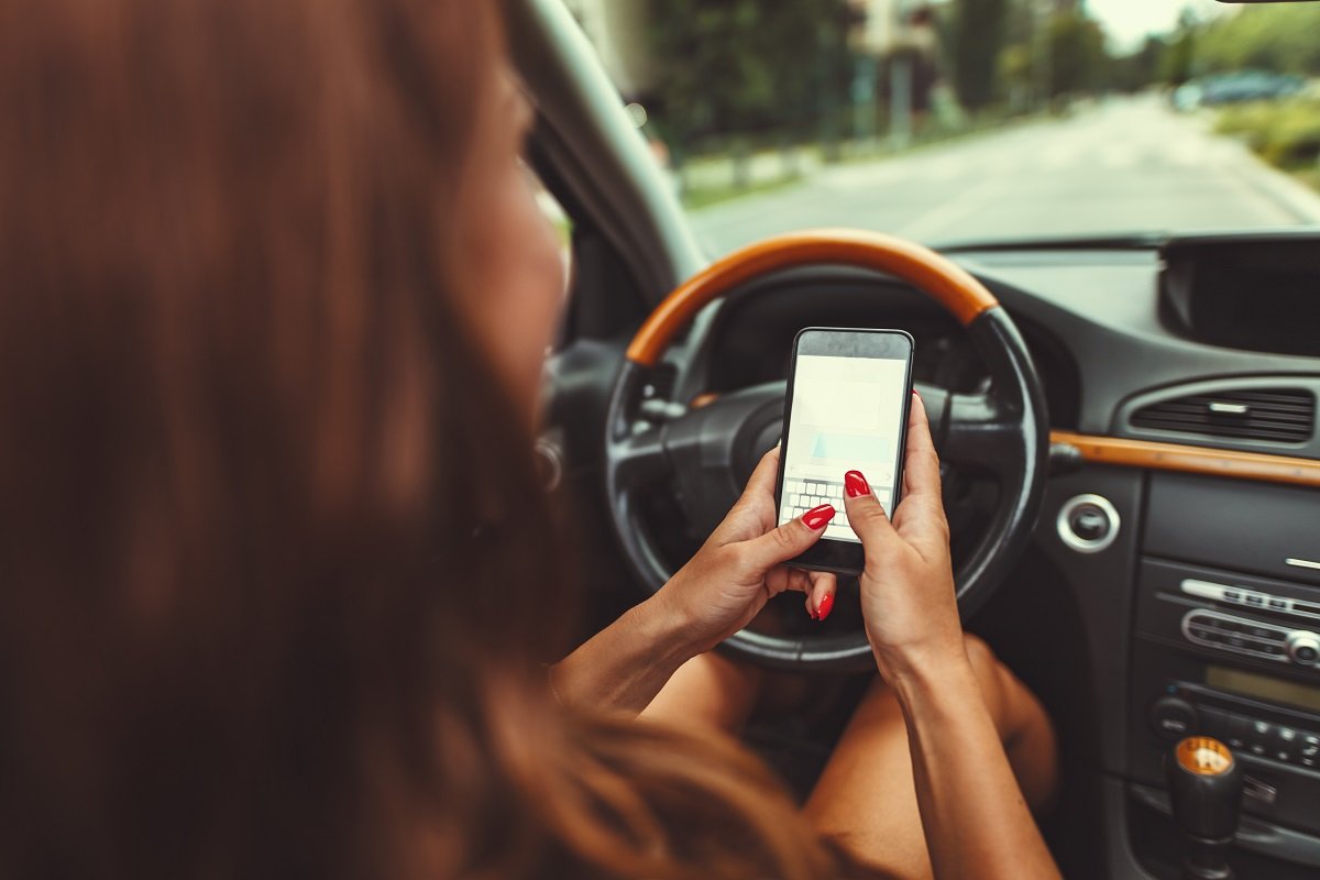 Woman is texting on smartphone while driving a car and leads herself to danger.