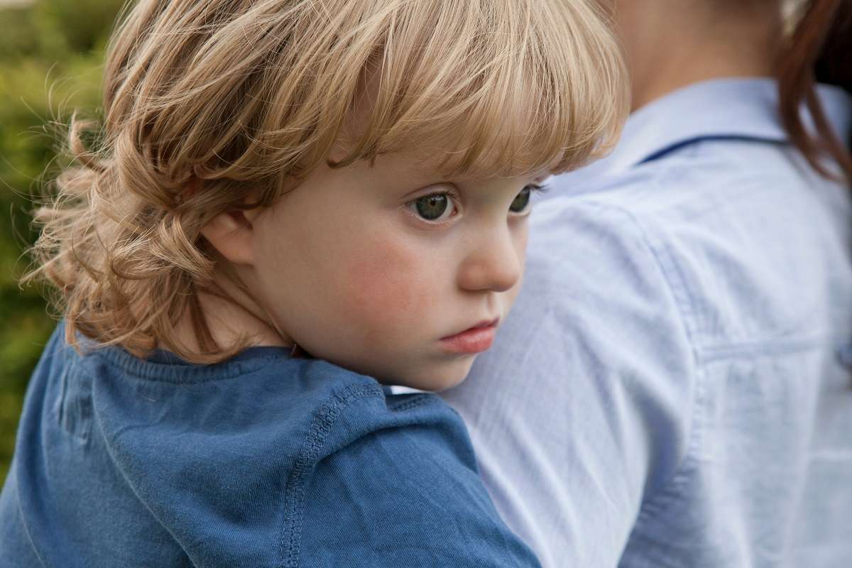 A sad child being carried by a parent