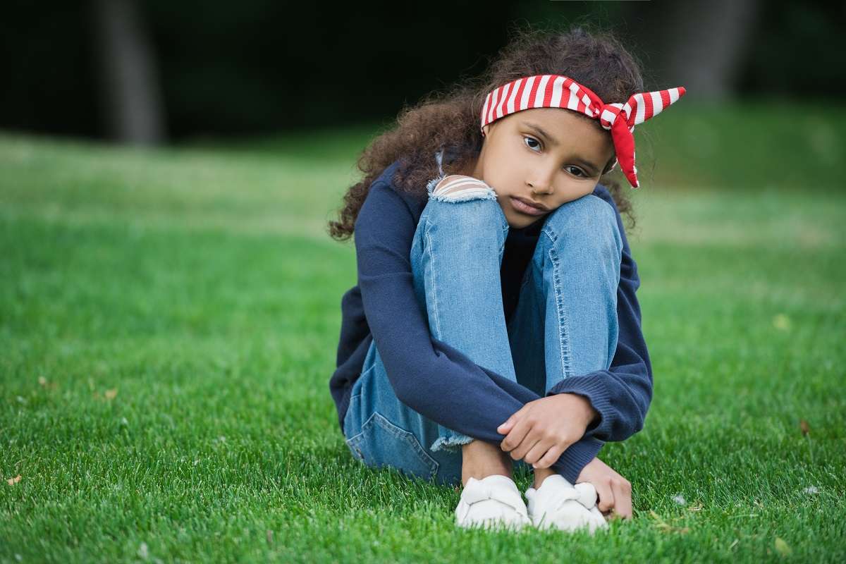 A sad little girl sitting on the grass