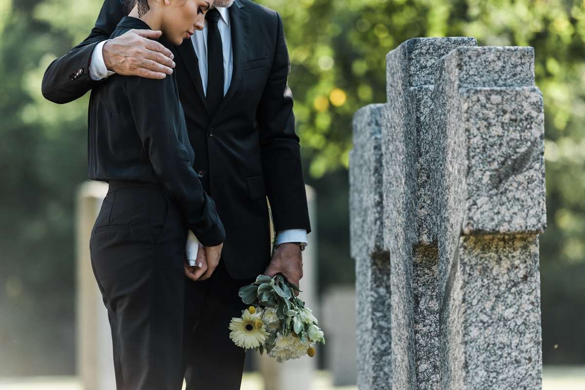 Two people at a graveside with flowers